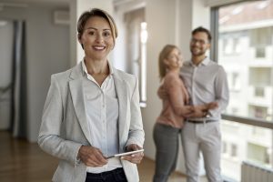 Portrait of female real estate agent looking at the camera while happy couple in standing in the background.
