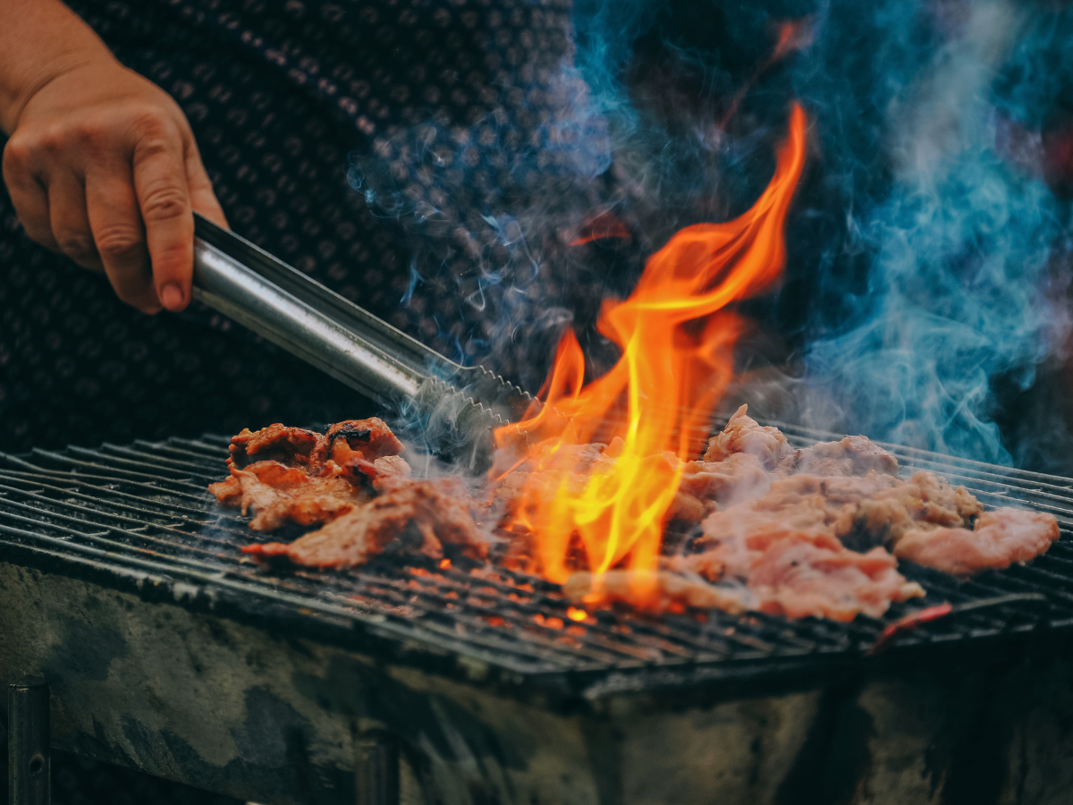Food cooking over an open barbecue with flames and smoke.