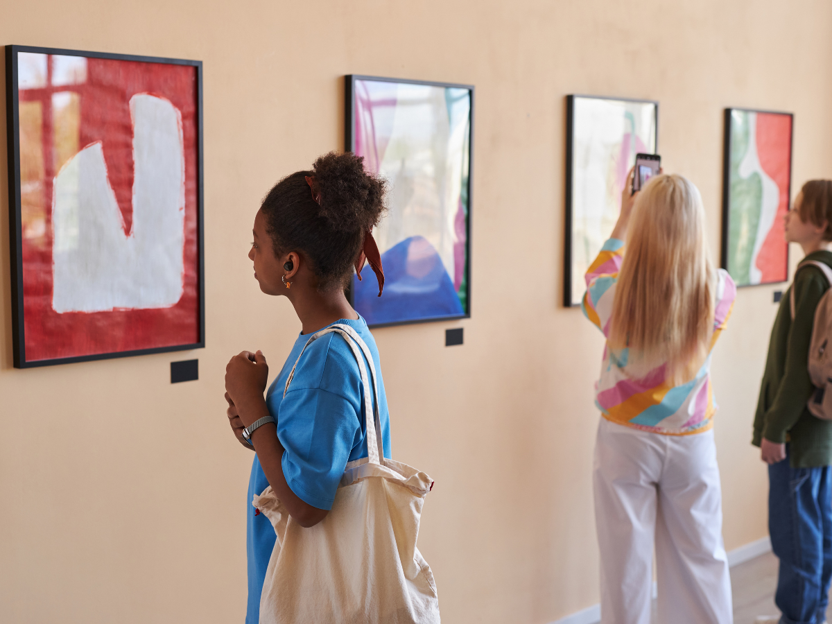 Visitors viewing colourful framed artworks in an art exhibition.