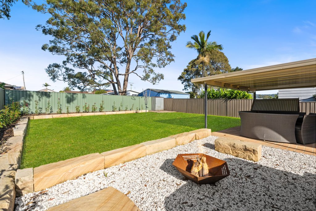 Landscaped backyard with fire pit, covered patio and level lawn at a Killarney Vale home